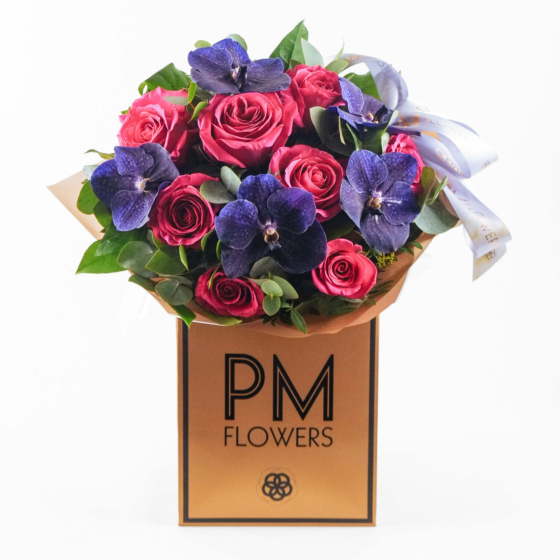 A bouquet of pink roses and purple vanda orchids with green leaves, wrapped in a gold-colored paper with the logo &