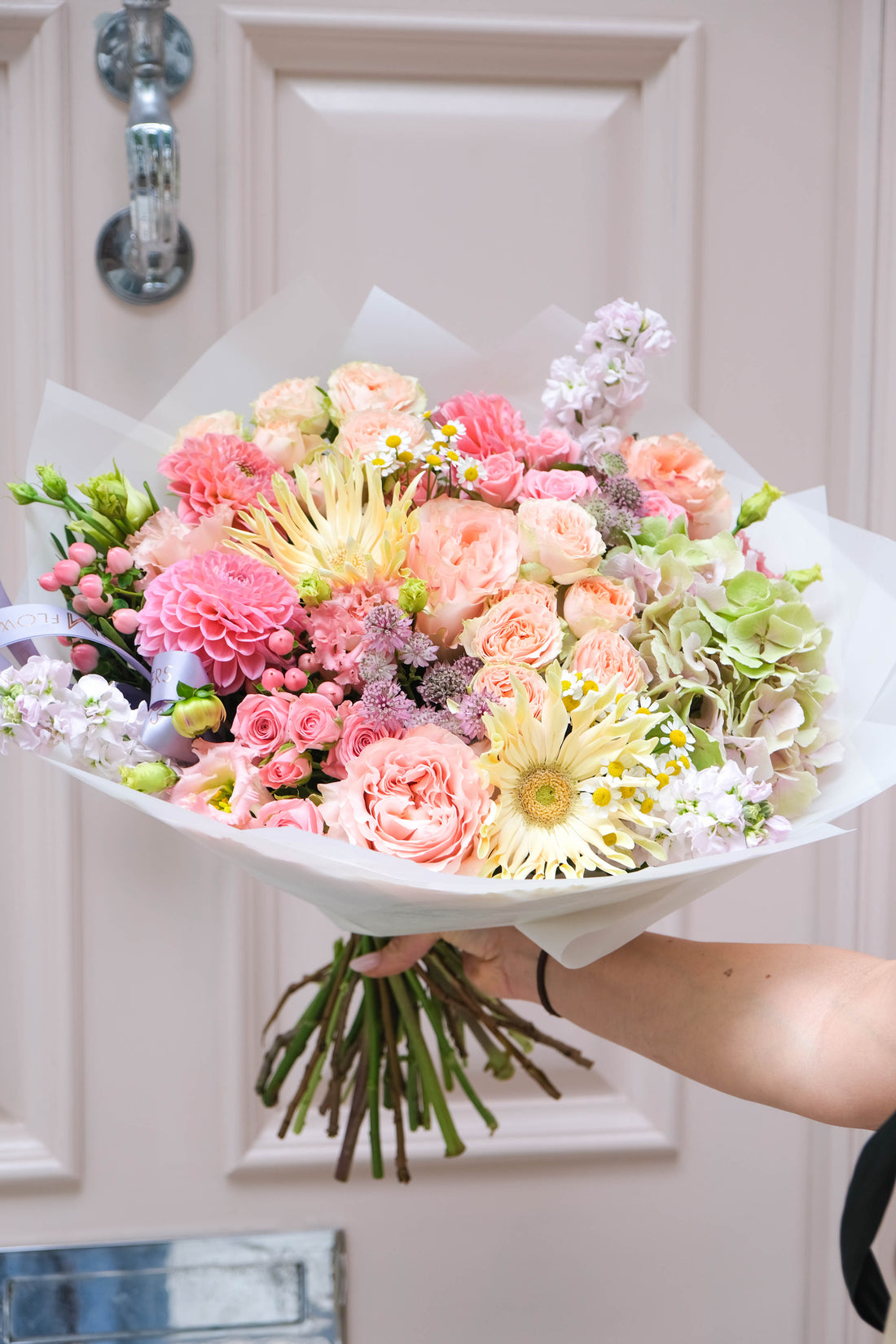 Bouquet of flowers held in front of a pastel door