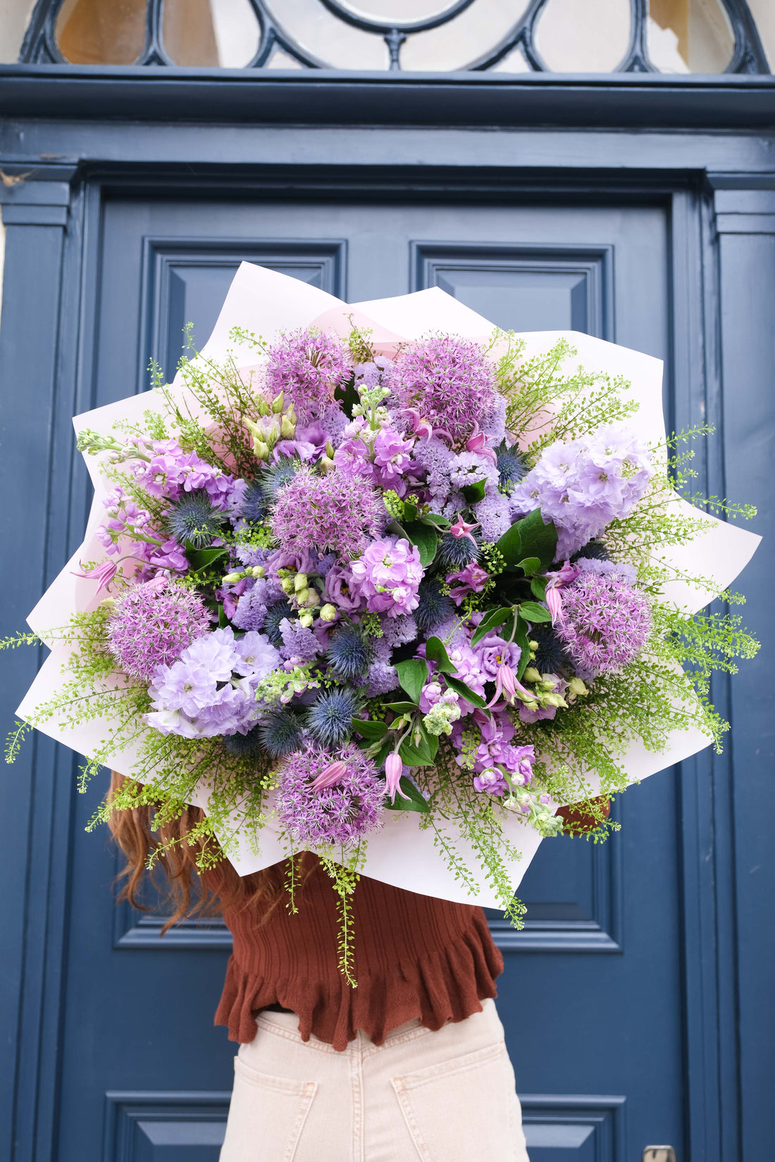 Bouquet of purple flowers held by a person in front of a blue door