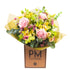 A freshly arranged floral bouquet with large dusky pink roses, orchids, and other summer flowers, wrapped in yellow and green paper with &