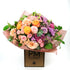 A vibrant bouquet of flowers featuring a mix of purple, pink, and orange blooms, wrapped in a peach-colored paper with &
