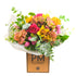 A colorful bouquet of assorted flowers including sunflowers, roses, and orchids, wrapped in paper with &