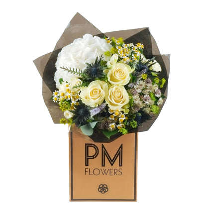 A bouquet of white flowers including roses and other foliage, wrapped in a brown paper with the logo &