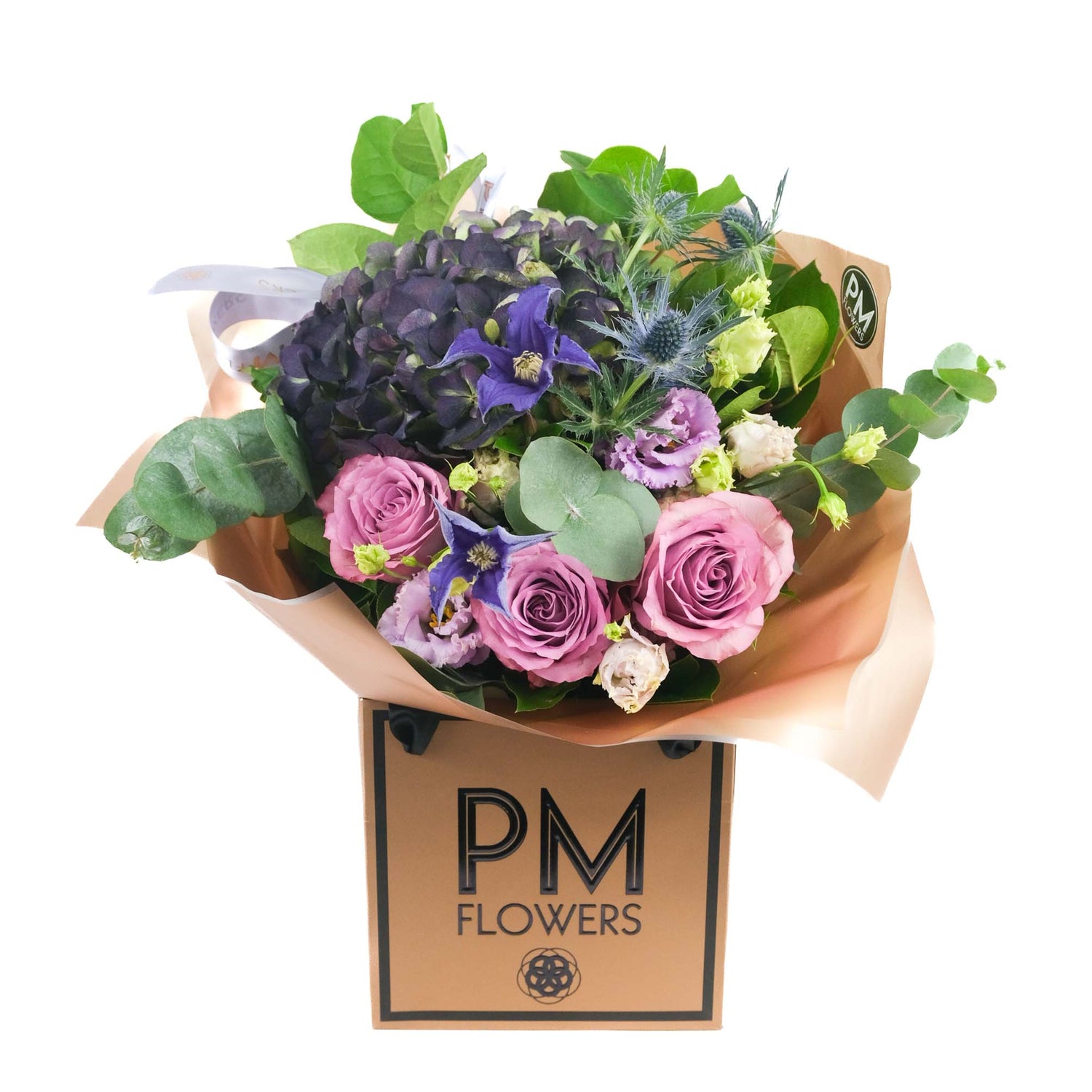 A bouquet of flowers including roses and hydrangeas in a mix of purple, pink, and green colors, presented in a rose gold wrap with &